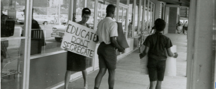 Black and white photo of someone holding a sign that says "Educate, don't segregate"